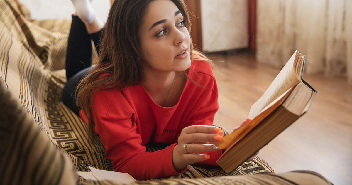 Come iniziare l'anno leggendo: giovane donna vestita di rosso legge un libro sdraiata su un divano