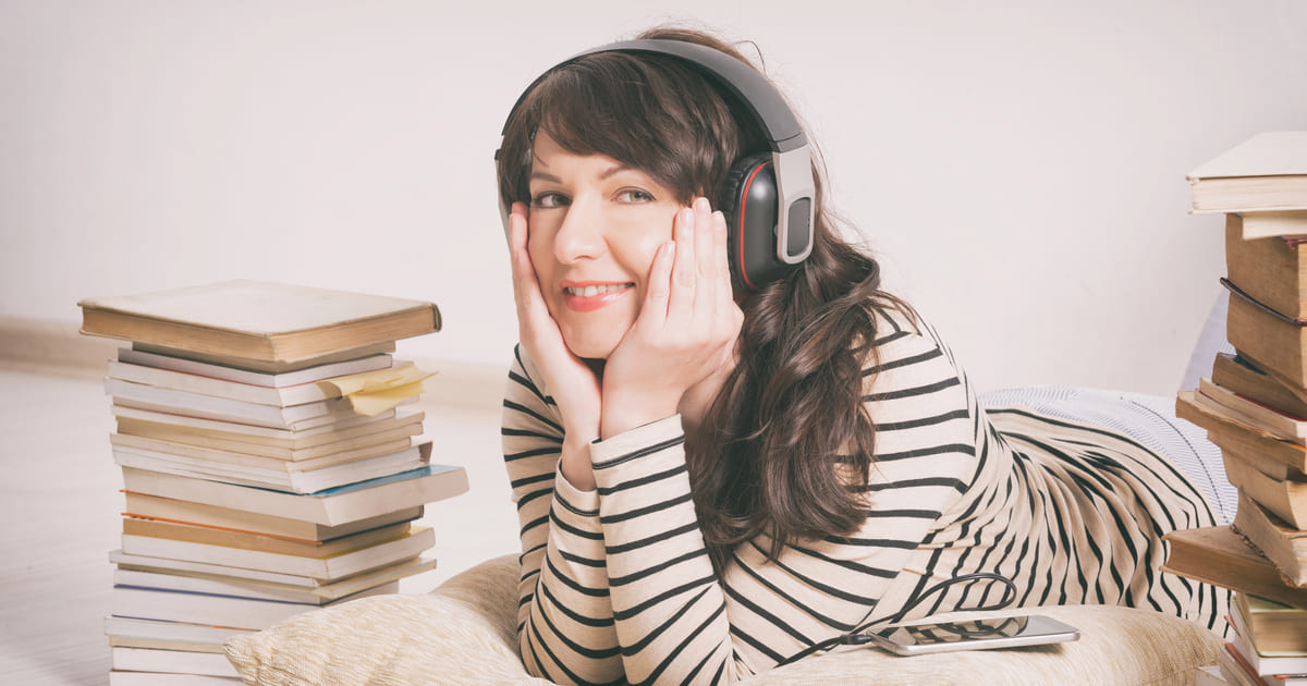 Differenze tra leggere e ascoltare: donna sdraiata a terra con cuffie e circondata da pile di libri