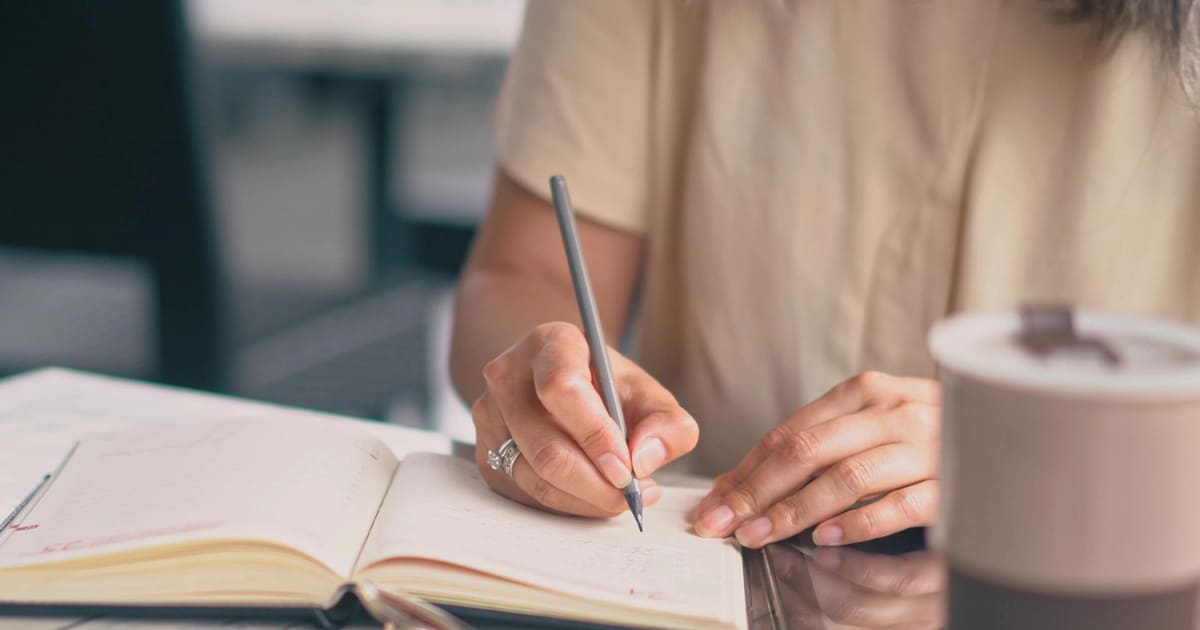 Donna scrive a mano su un quaderno per creare personaggi memorabili per i suoi romanzi