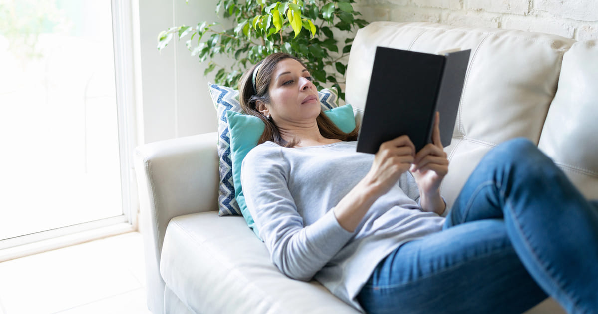 Citazioni sulla lettura: una donna legge un libro sdraiata su un divano grigio