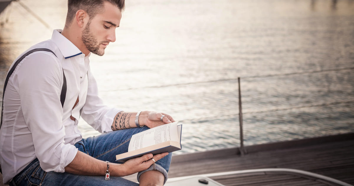Uomo legge un libro all'aperto vicino all'acqua: un modo per libri per viaggiare senza muoversi.