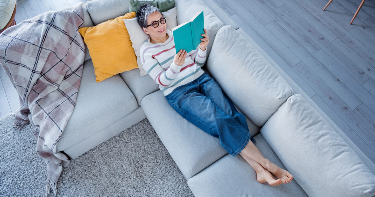 Donna rilassata sul divano che legge un libro, ideale per i classici da leggere in un fine settimana brevi e veloci.