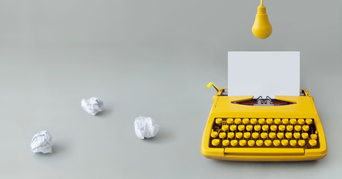 Macchina da scrivere gialla con foglio bianco e carta accartocciata che rappresenta le frasi sul blocco dello scrittore