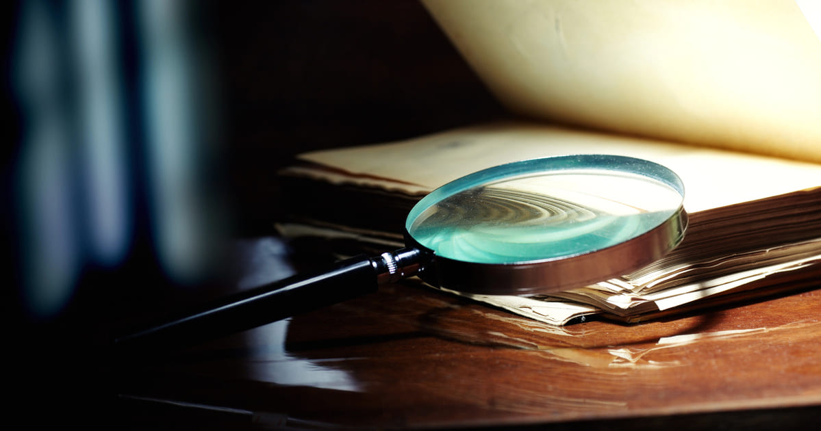 Lente d'ingrandimento su libro antico che rappresenta i migliori gialli di sempre tra letteratura e cinema investigativo