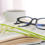 Libro aperto con fiori primaverili, occhiali e tazza di caffè — consigli di lettura marzo 2026