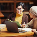 Due donne adulte studiano insieme in biblioteca con laptop e libri, esempio di biblioteche e apprendimento permanente