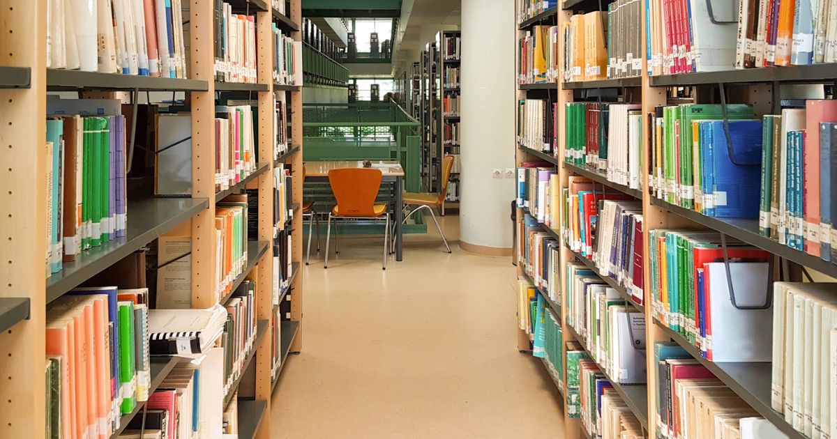 Corridoio tra scaffali di libri in una biblioteca moderna: il ruolo della biblioteca oggi come spazio di accesso alla conoscenza