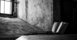 Un libro aperto e un paio di occhiali su un tavolo di legno in una cella, esempio di libri scritti in carcere.