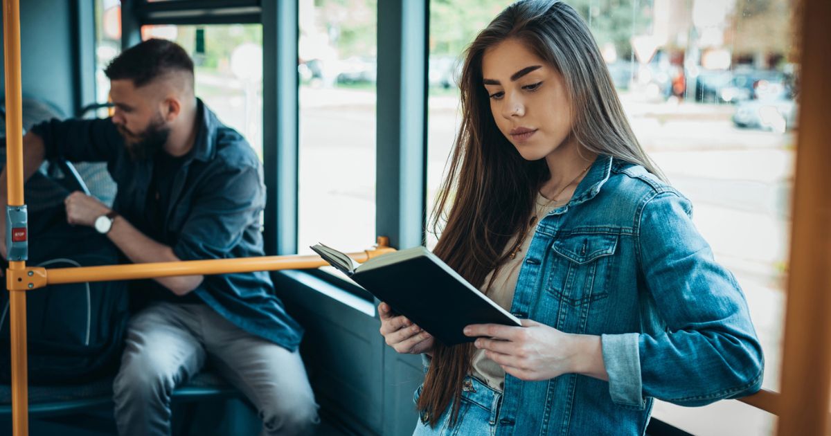 Una giovane donna legge un libro classico in piedi su un autobus affollato, a dimostrazione del perché leggere i classici oggi.