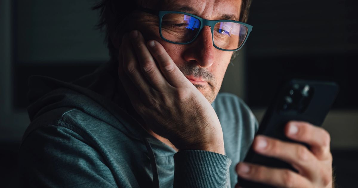 Un uomo guarda lo smartphone di notte con espressione ansiosa, simbolo della FOMO e della paura di essere esclusi