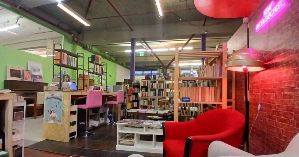 Lo spazio di New World Bordel ad Amsterdam: poltrone, postazioni di coworking e l'insegna al neon con il nome della biblioteca