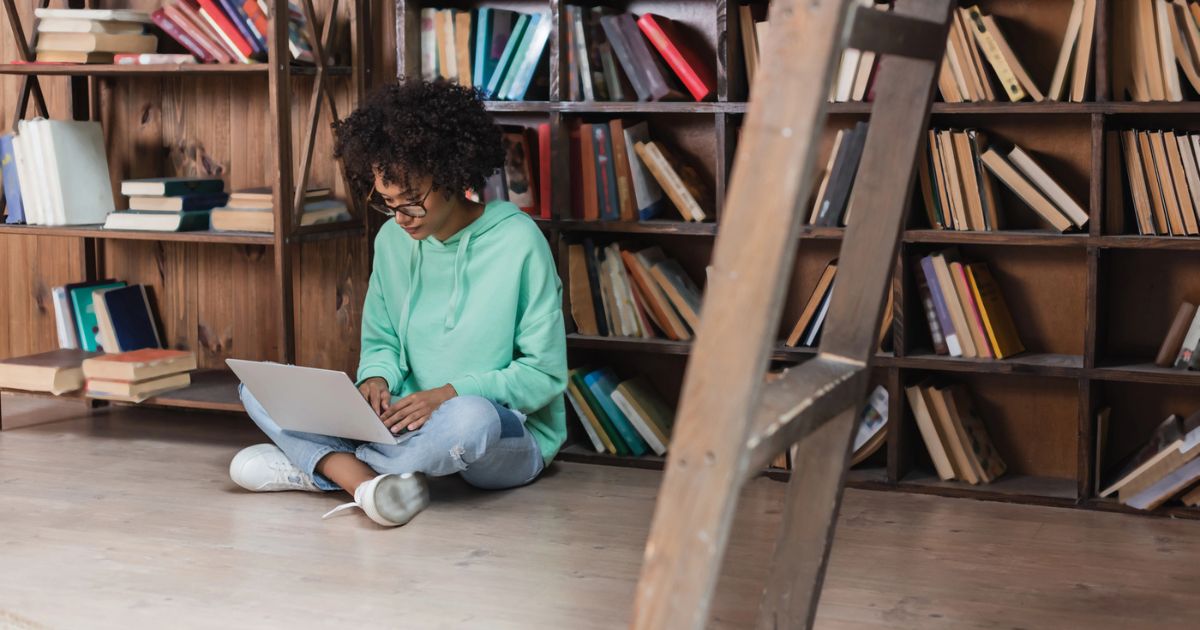 Ragazza con laptop seduta tra gli scaffali di una biblioteca — biblioteche e intelligenza artificiale