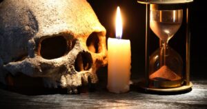Frasi sul memento mori: teschio, candela accesa e clessidra su sfondo scuro